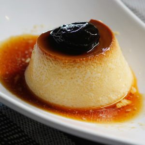 Appetizing caramel flan dessert with a rich prune topping served in a white dish.