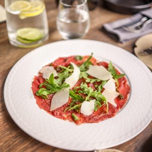 A delectable carpaccio dish garnished with arugula and parmesan, perfect for a gourmet meal.