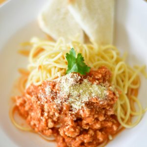 Plate of spaghetti bolognese topped with cheese and parsley, served with bread slices.