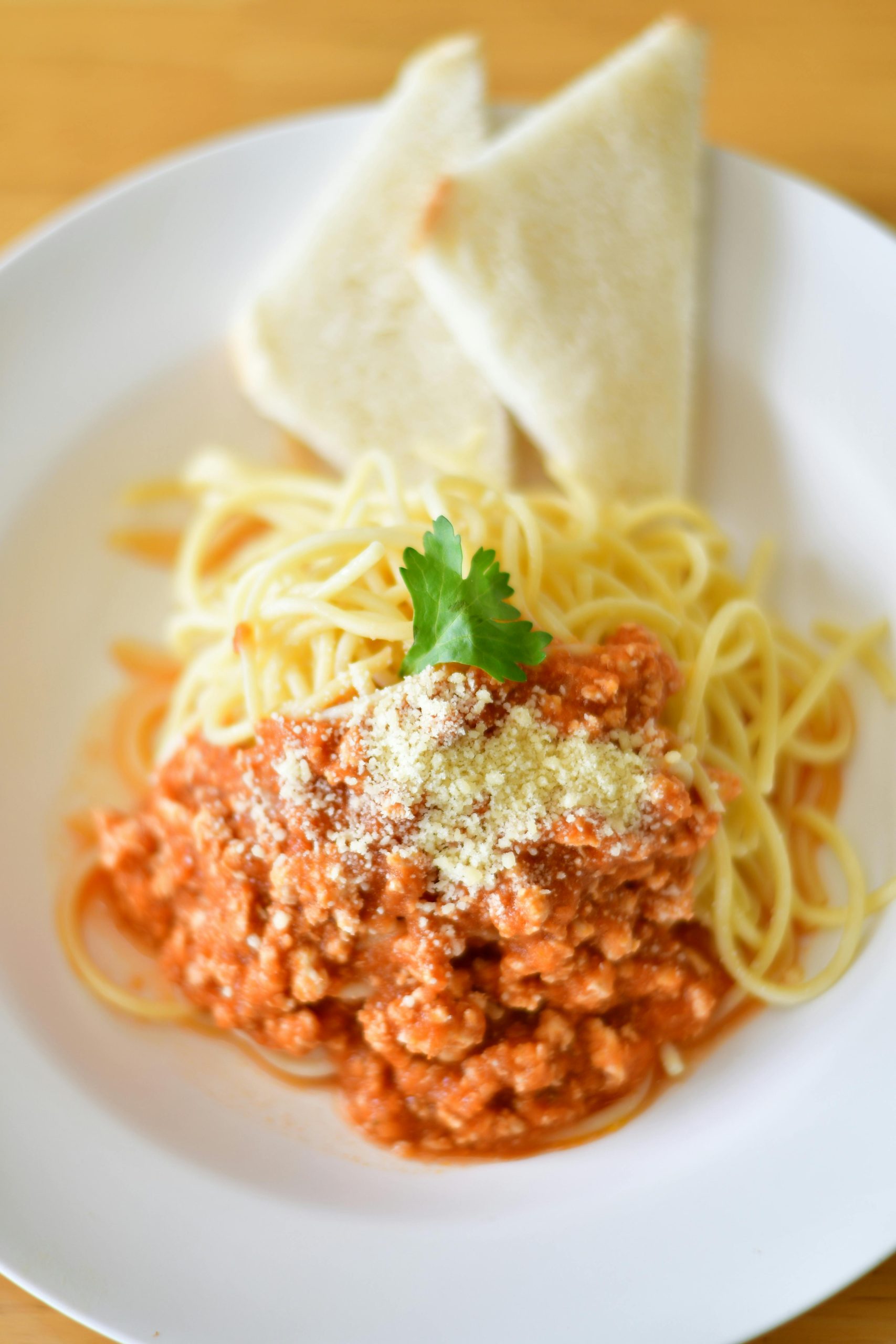 Plate of spaghetti bolognese topped with cheese and parsley, served with bread slices.