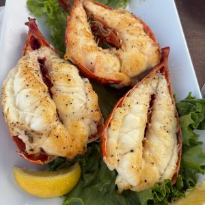 Delicious grilled lobster tails served with lemon slices and fresh greens, perfect for a seafood feast.