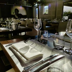 Sunlit restaurant table setting with wineglasses and cutlery, creating a warm dining atmosphere.