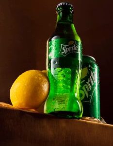 Sprite bottle and can with fresh lemon and water droplets for a vibrant visual.